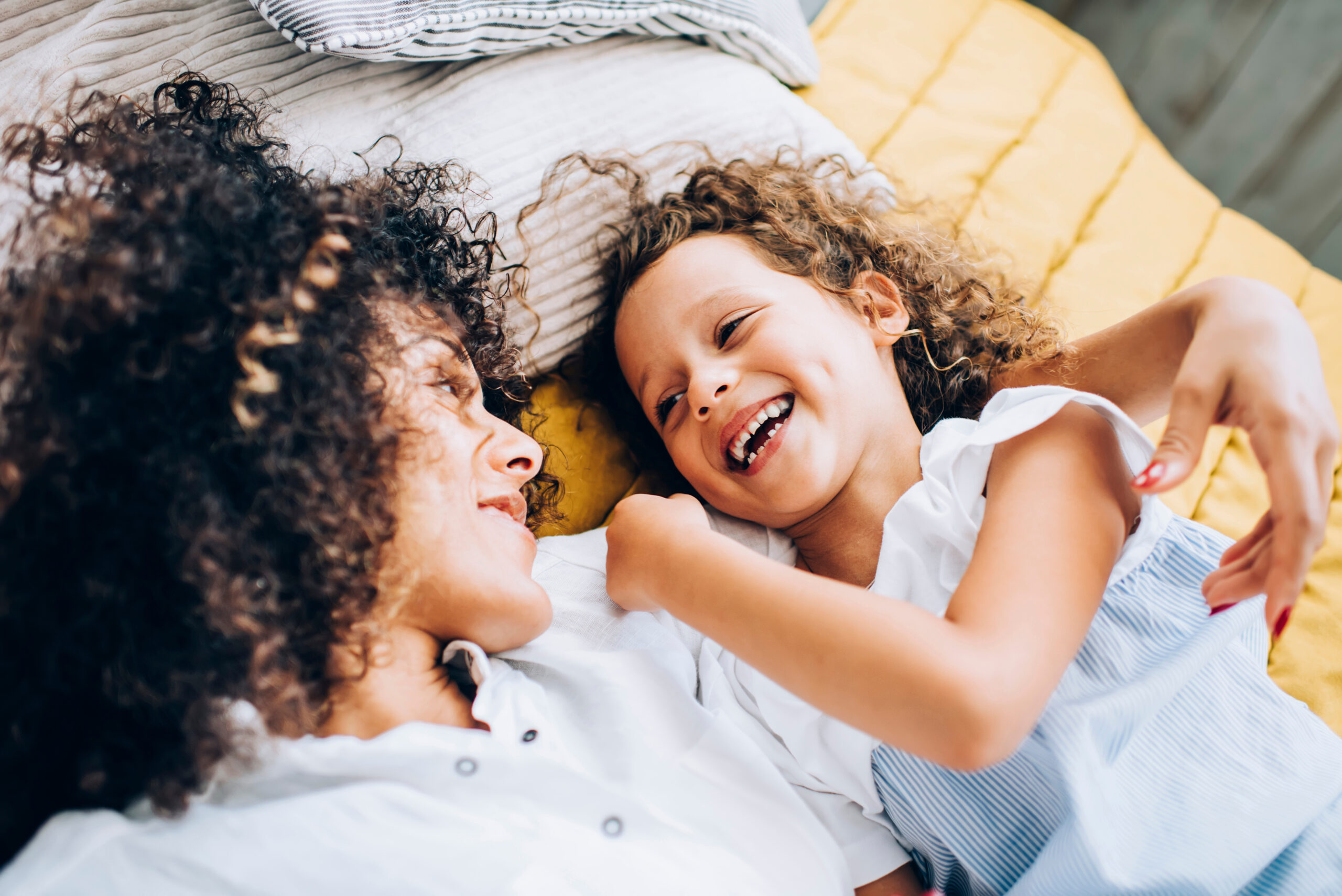 Laughing happy girl with mother on bed